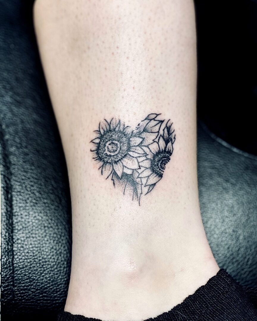 A black and white tattoo of a heart with sunflowers.