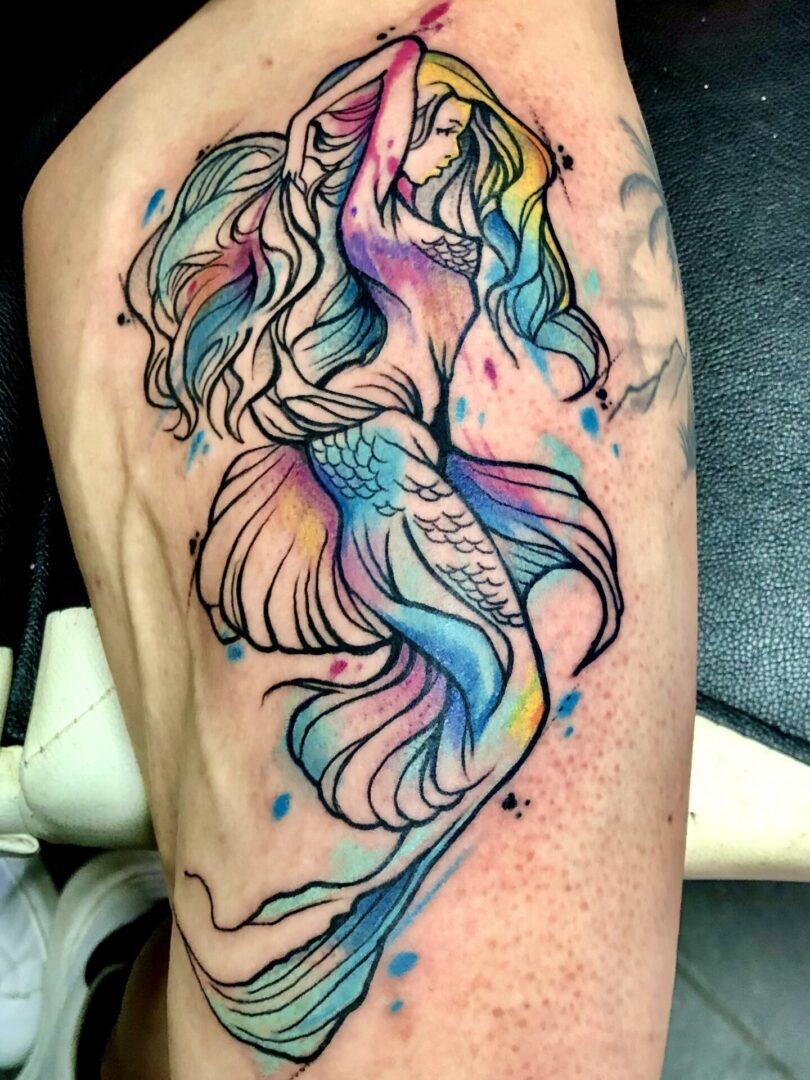 A colorful mermaid tattoo on the arm of a woman.