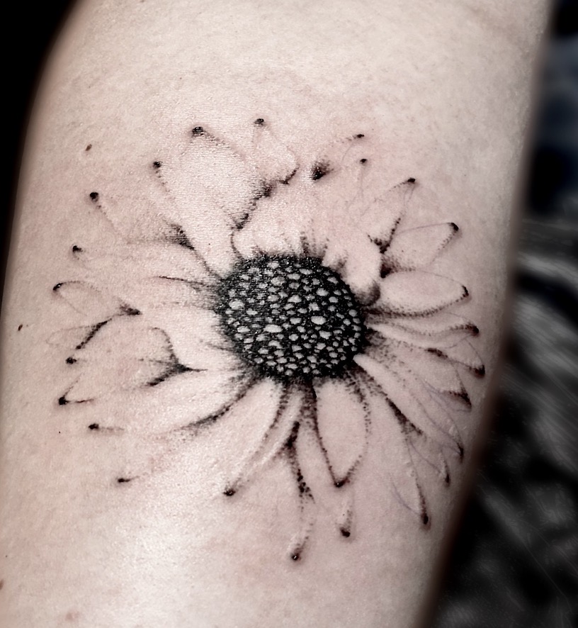 A tattoo of a flower with black dots on it.