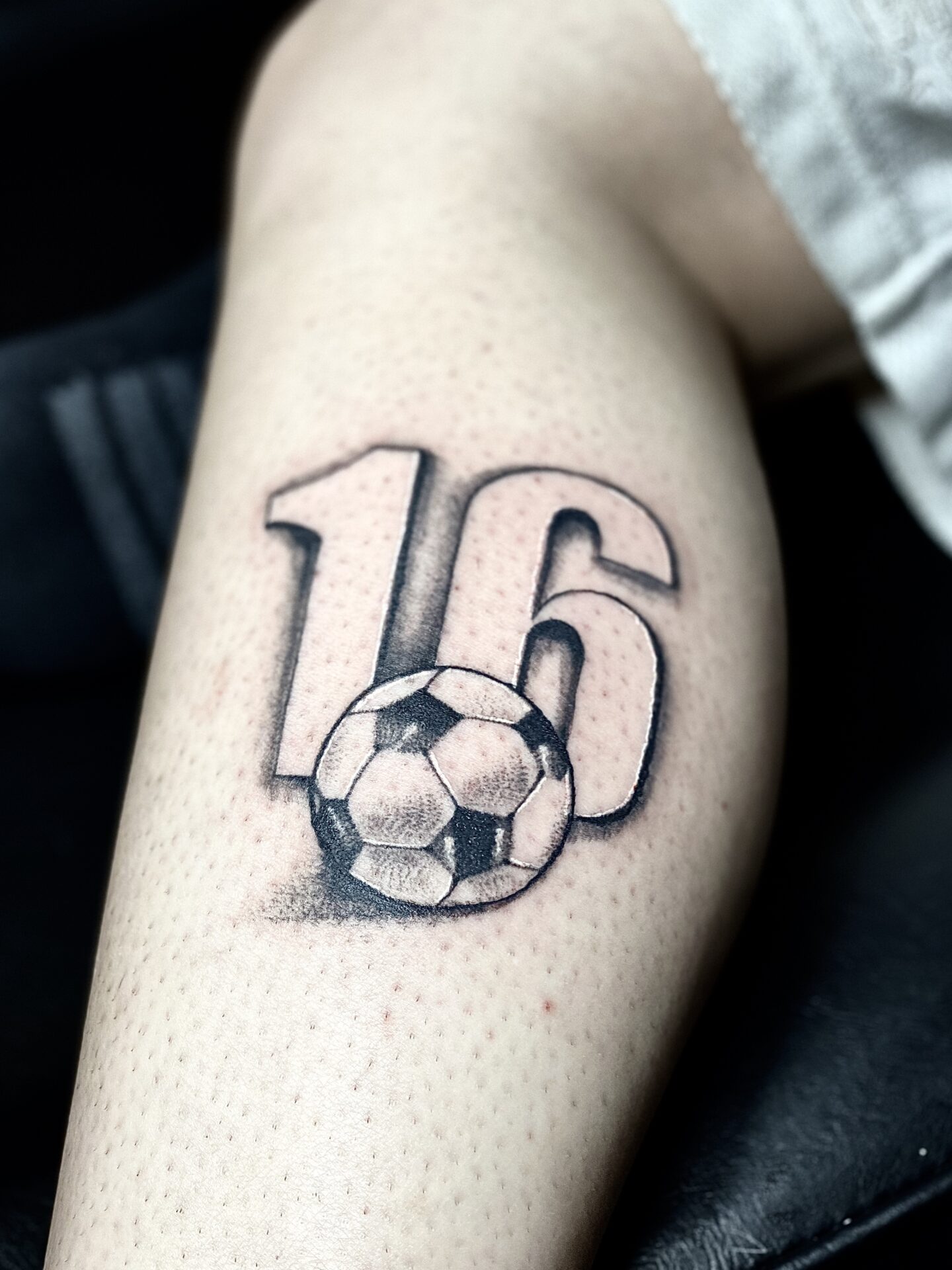A tattoo of a soccer ball with the number 1 6 on it.