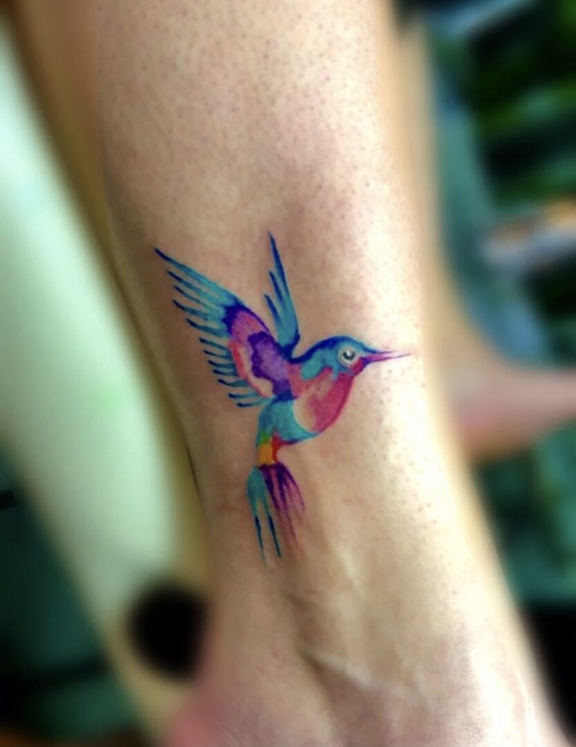 A hummingbird tattoo is shown on the arm.