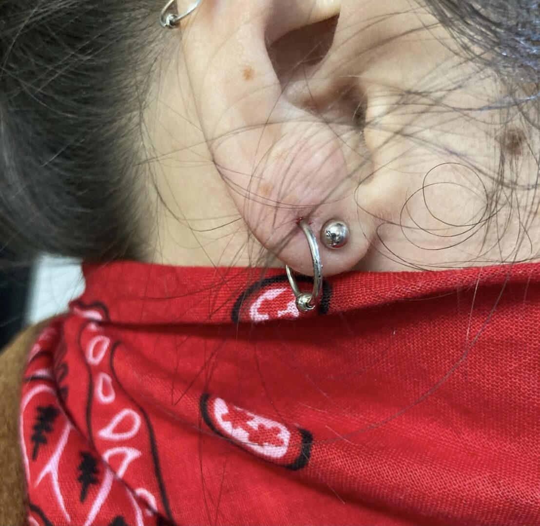 A woman wearing a red scarf with her ear piercings.