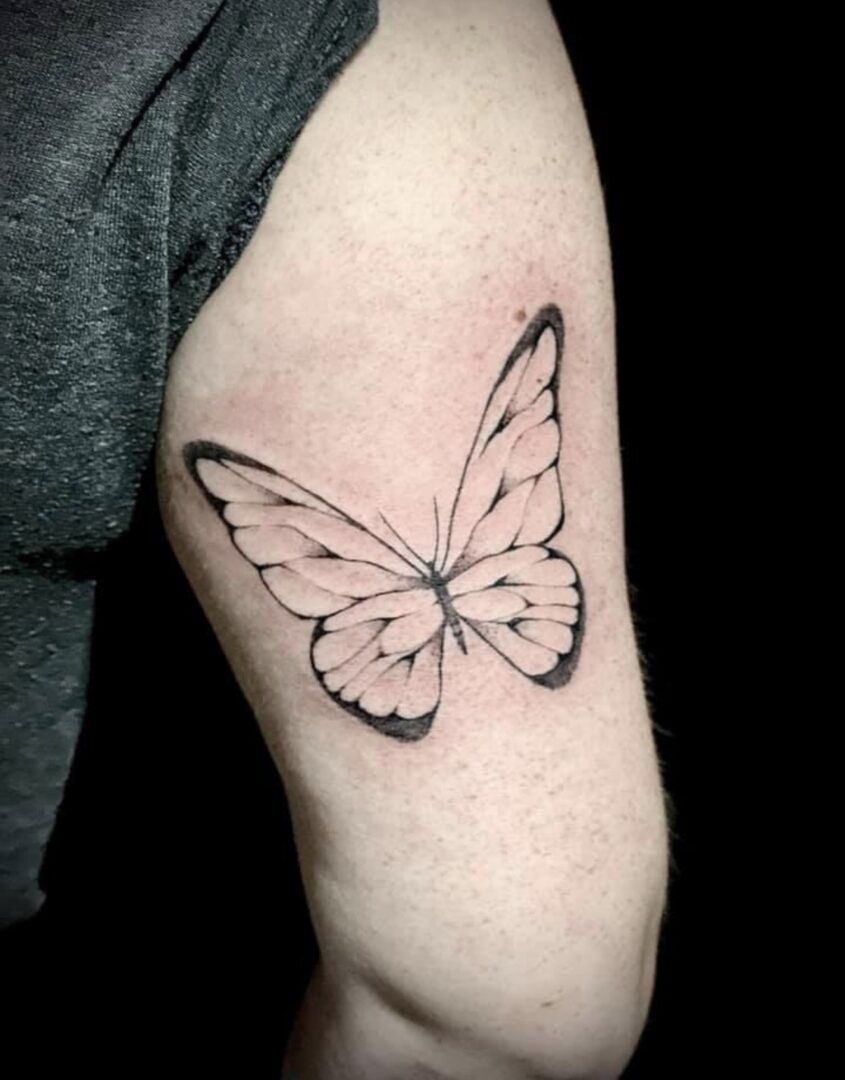 A black and white butterfly tattoo on the arm of someone.