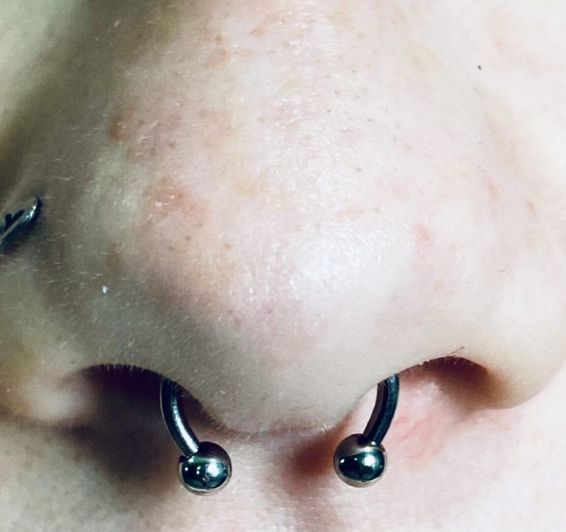 A person with their nose pierced with black balls.