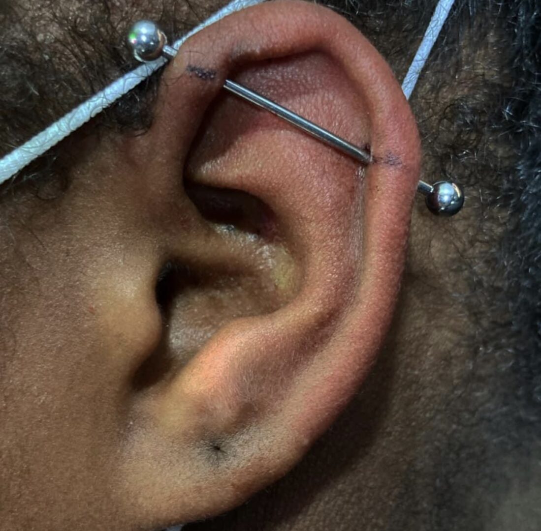 A person with their ear pierced and holding two needles.