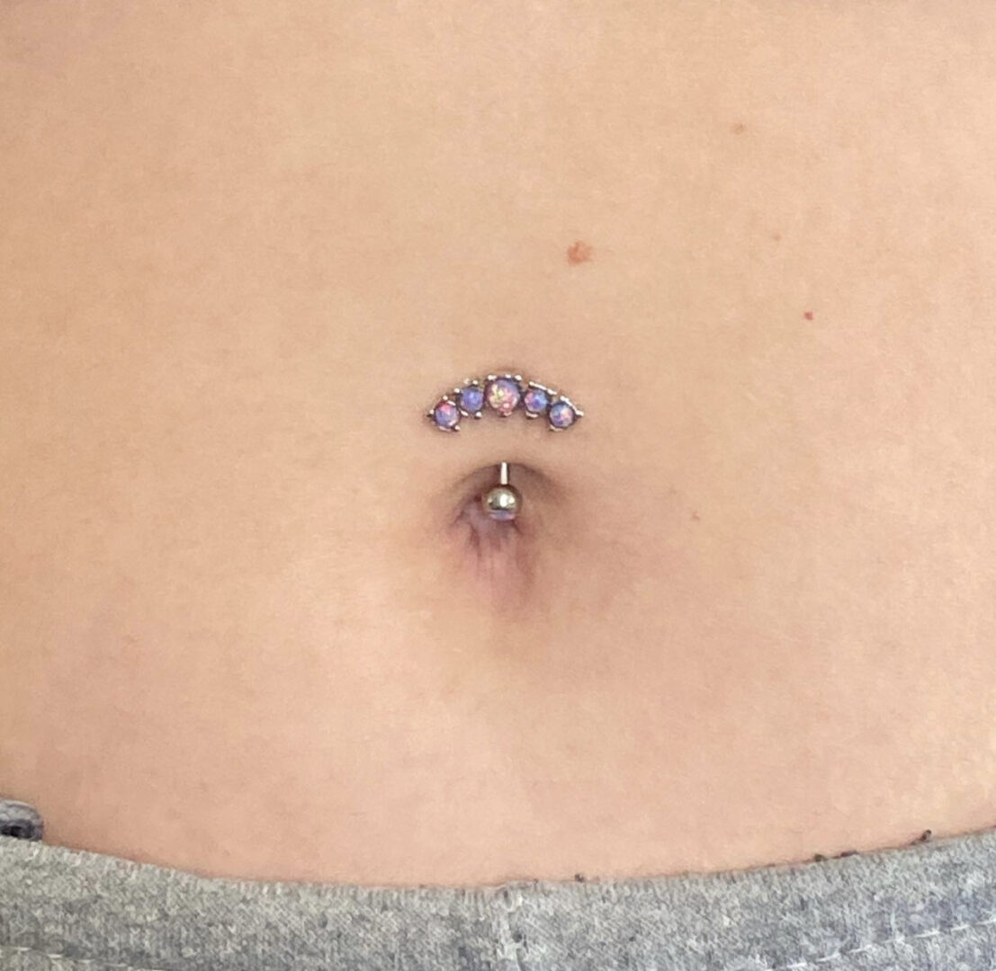 A woman with a belly button piercing and a small purple stone.