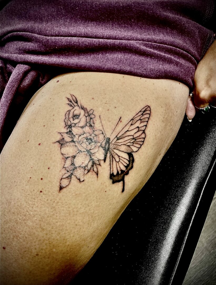 A woman sitting down with her leg up and a butterfly tattoo on it.