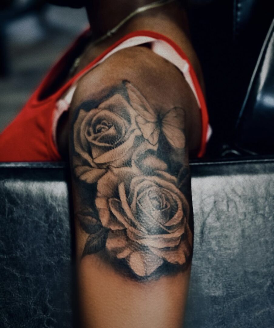 A woman sitting on the couch with her arm and shoulder tattoo of roses.