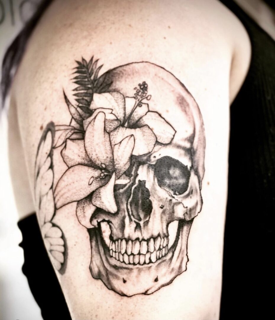 A black and white tattoo of a skull with flowers