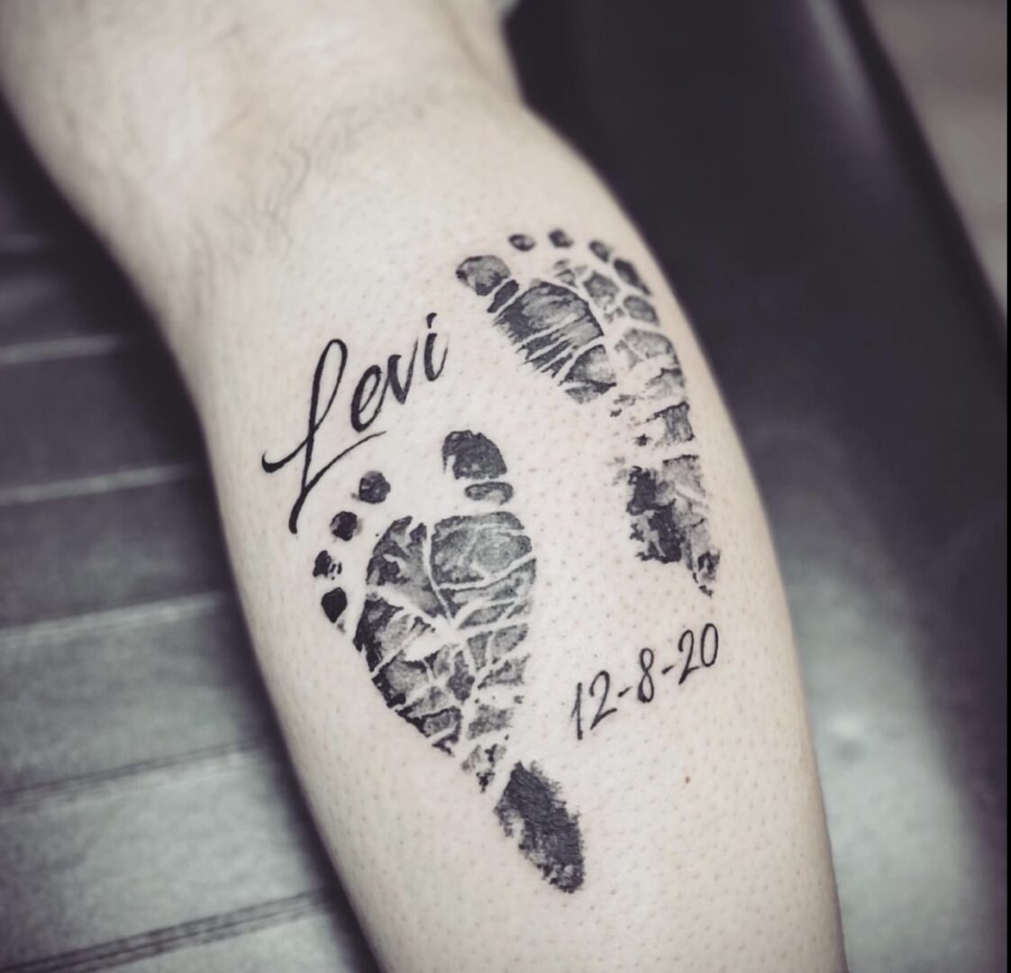 A tattoo of two feet with the name levi and date.
