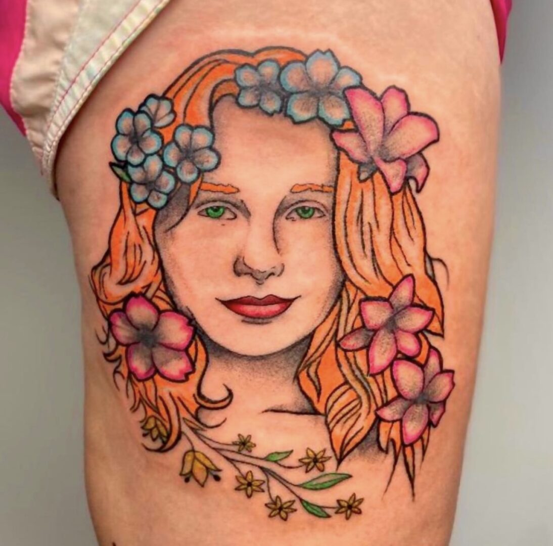 A woman with flowers in her hair is tattooed on the side of her leg.
