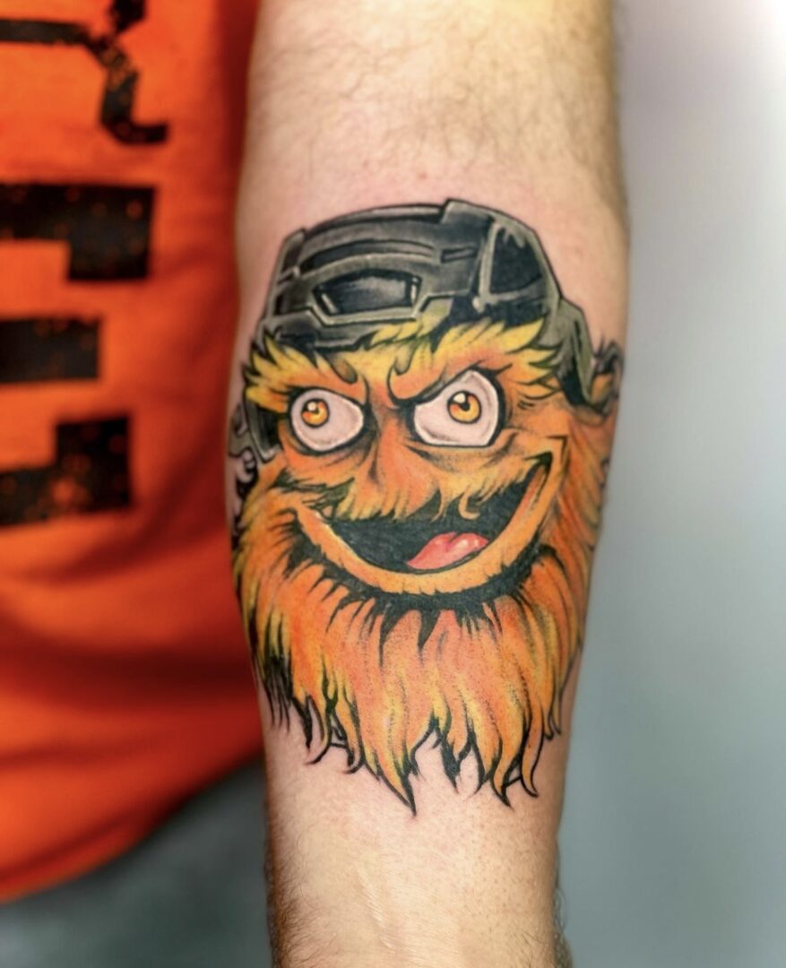 A tattoo of an orange monster with a hockey helmet on it's arm.