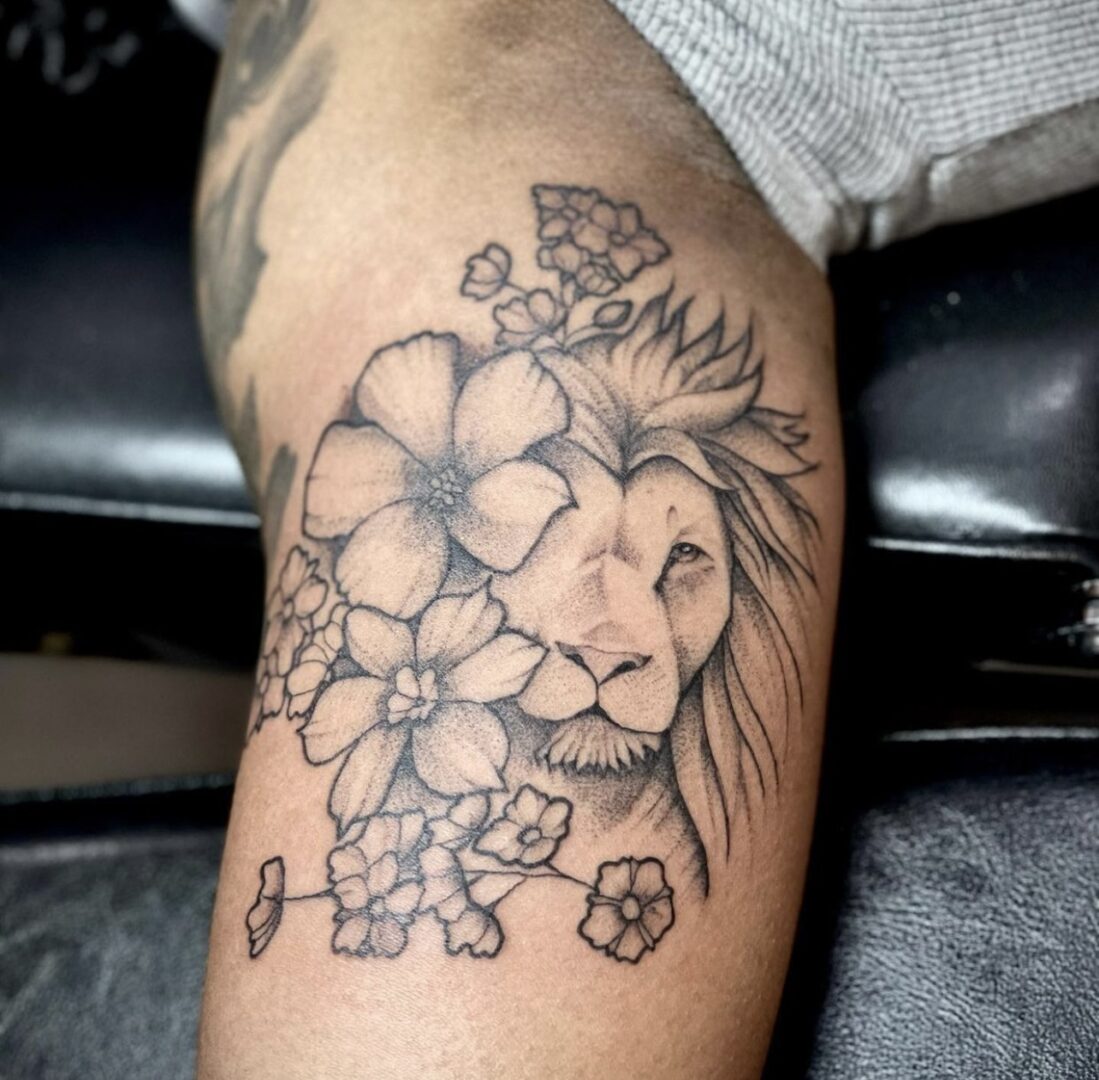 A tattoo of a lion with flowers on it's arm.