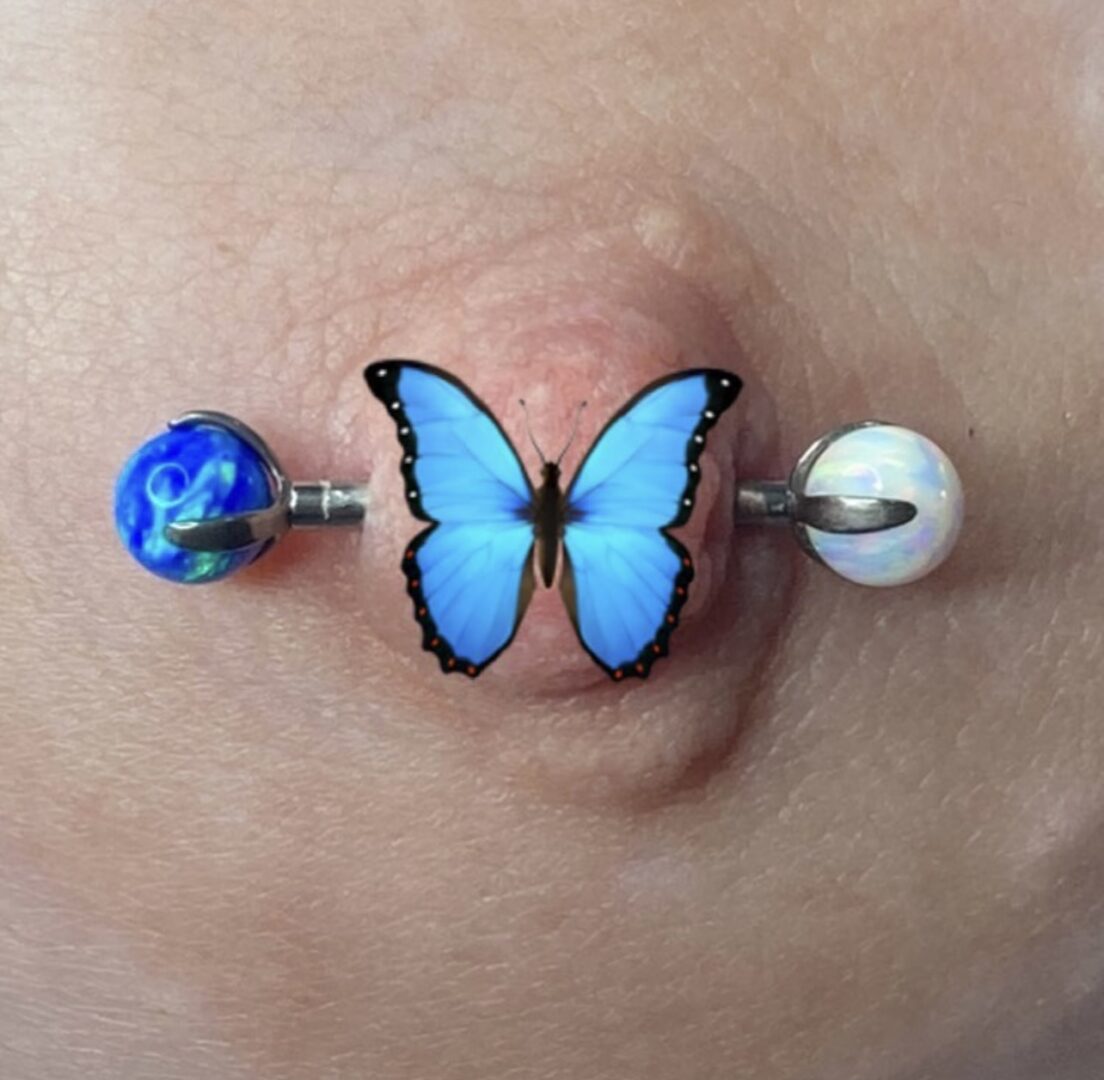 A blue butterfly piercing is shown on the side of a woman 's breast.