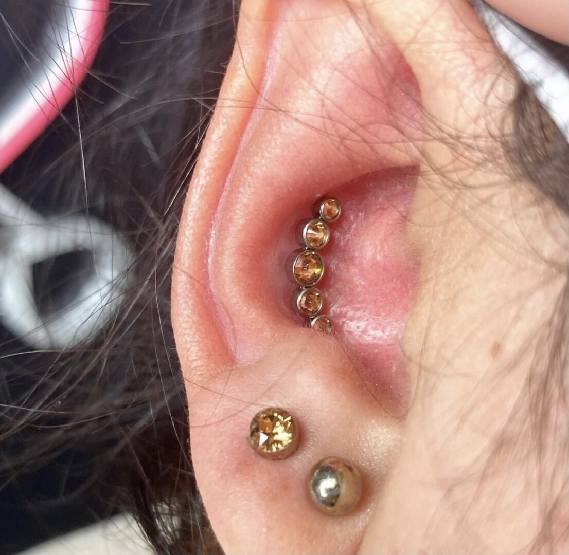 A person with their ear piercings and a gold ball earring.