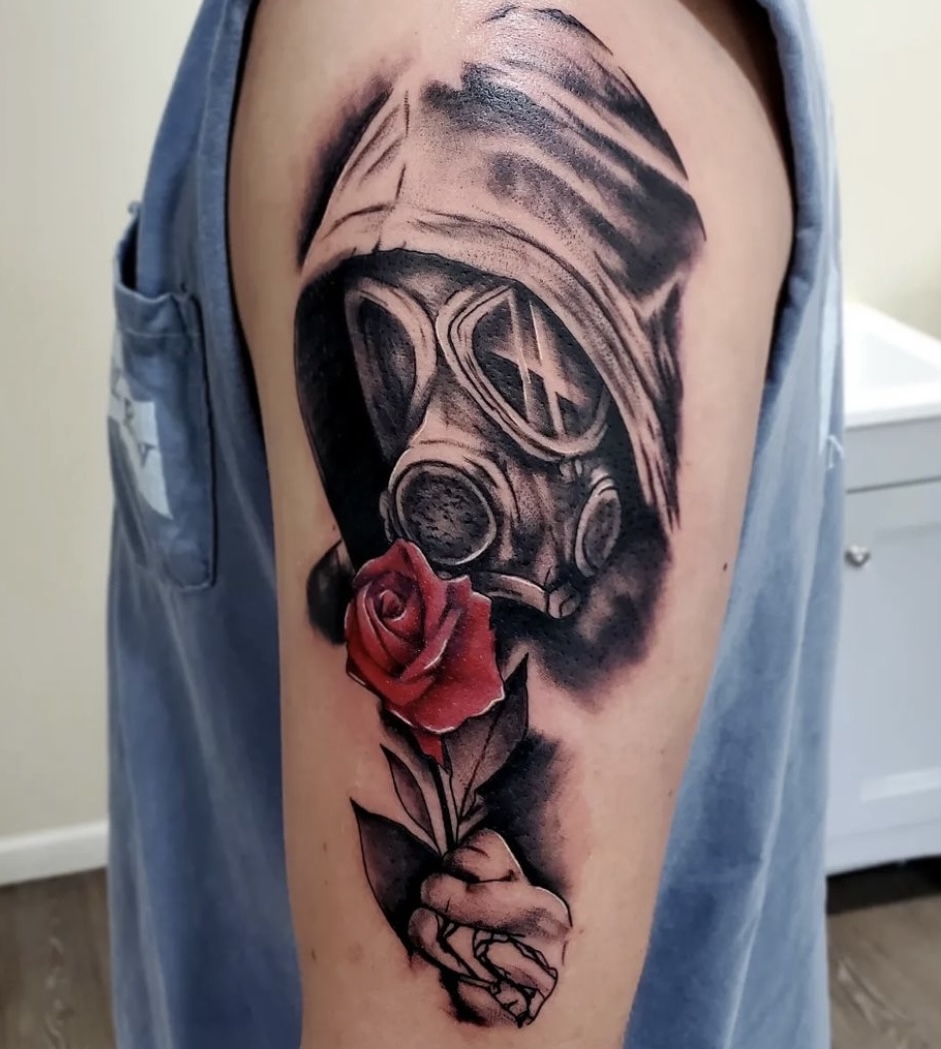 A man with a gas mask and rose tattoo on his arm.